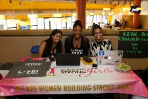 Gamma Phi Beta sisters sitting with a banner that says "We are women building strong girls."
