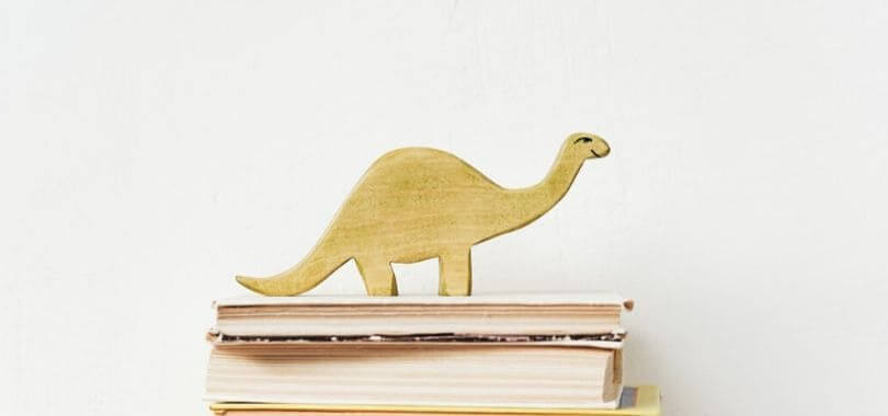 A wooden dinosaur on top of a stack of books.