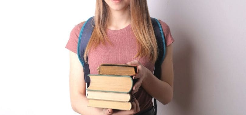 A student holding a stack of books with both hands.