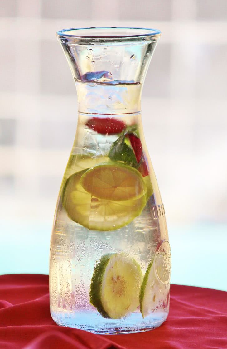 A pitcher filled with water with a slice of lemon inside.