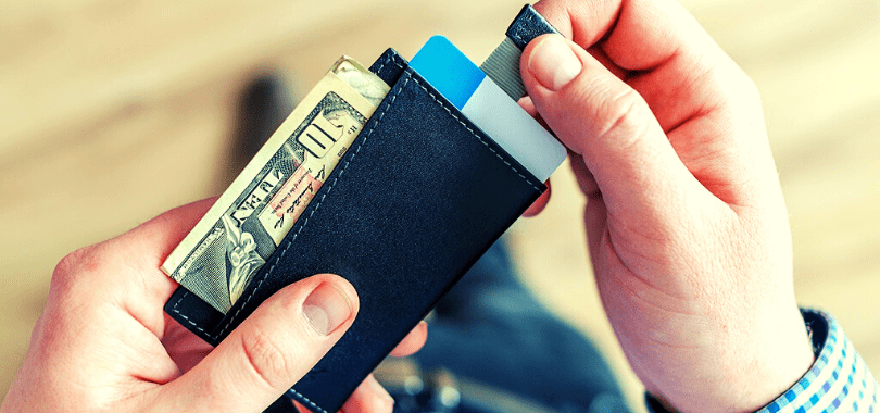 A student holding their wallet with a ten dollar bill sticking out of it.