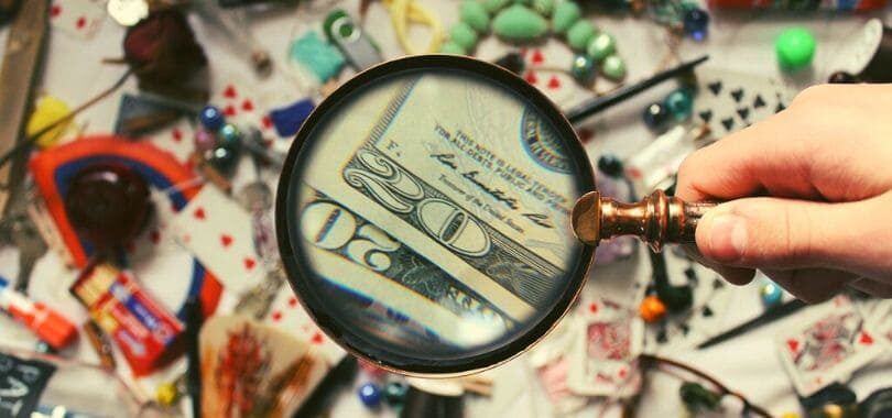 A magnifying glass pointed towards many items, with twenty dollar bills magnified.