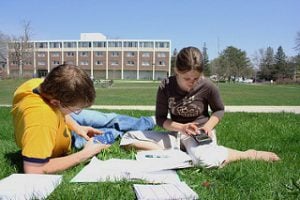 Two students studying outside on a blanket surrounded by books.
