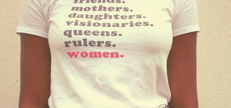 A person wearing a graphic t-shirt that says "...mothers, daughters, visionaries, queens, rulers, women."