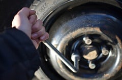 Hand holding a wrench attached to lug nut of the tire .