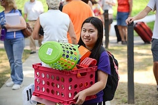 Student carrying her dorm supplies in a pink basket while moving into college.