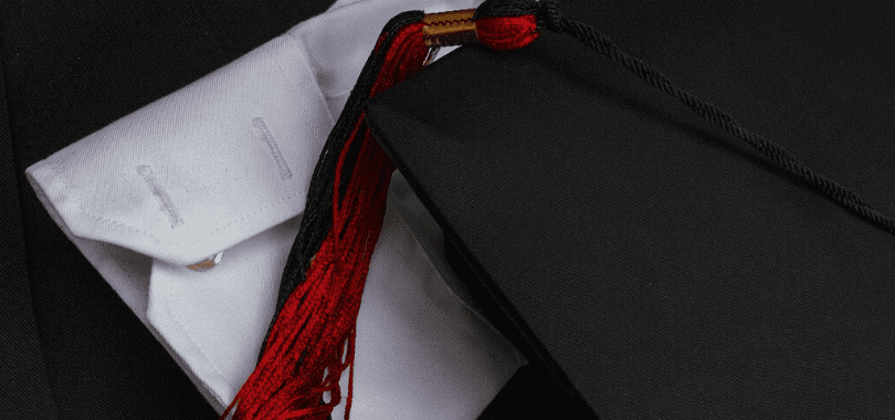 A graduation cap with a red tassel laying on top of a white shirt sleeve.