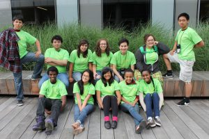 Twelve students posing for a picture, all wearing a green shirt.