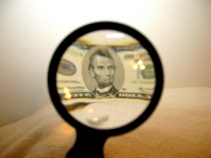A five-dollar bill shown in a magnifying glass.