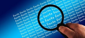 A hand is holding a magnifying glass over a bunch of text that says "facts."