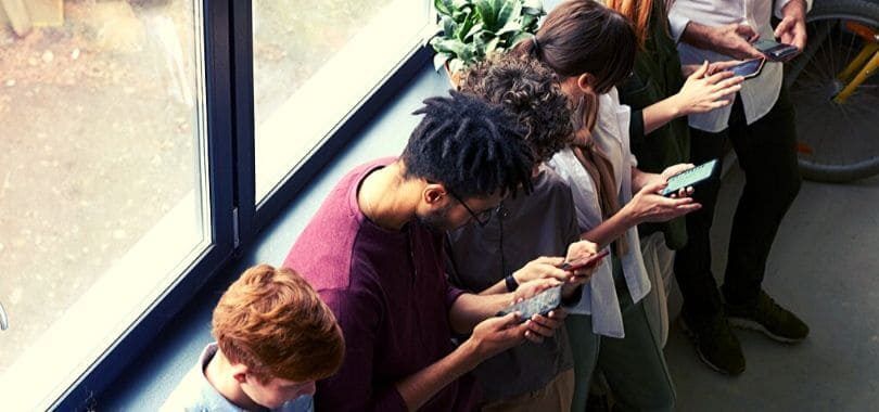 Students leaning against a window ledge on their phones.