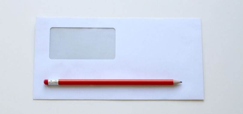 An empty white envelope with a red pencil sitting on top of it.
