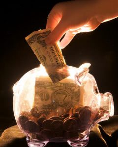 Hand dropping a dollar bill in a transparent piggy bank.