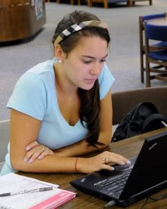 Female college student scrolling through her laptop and studying in the library.