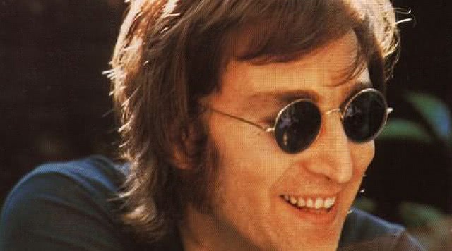 John Lennon is smiling and wearing shades.