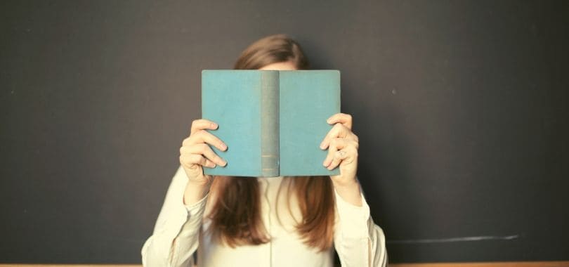 A person holding an open book in front of their face.