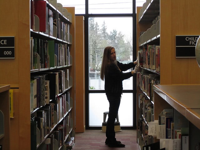 A woman standing between two shelves looking for a book.
