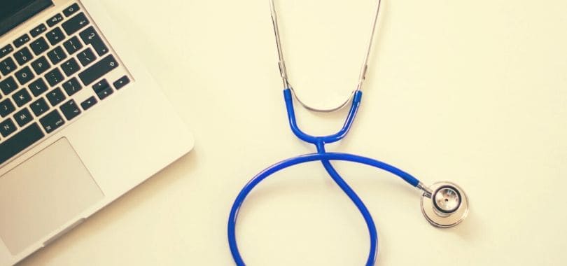 A blue stethoscope next to a laptop.