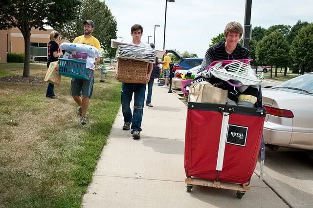 Three college students are carrying their dorm supplies while moving into college.