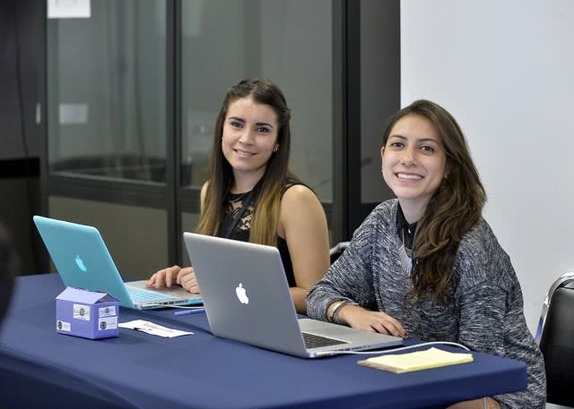 Two smiling female students with their laptops on the desk.