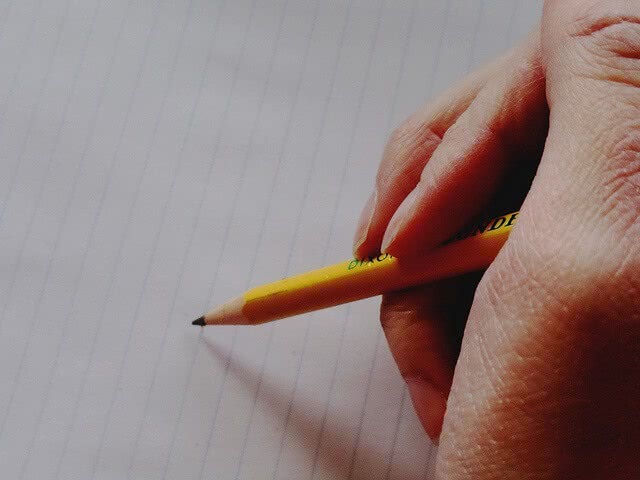 A hand holding a pencil ready to write on lined paper.