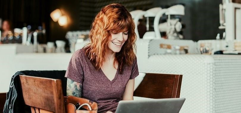 College student smiling as she works on her laptop in a coffee shop.