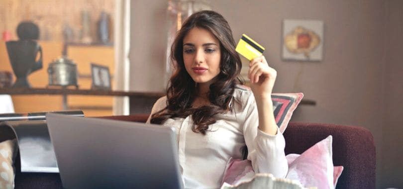 A woman sitting on a couch holding a yellow credit card.