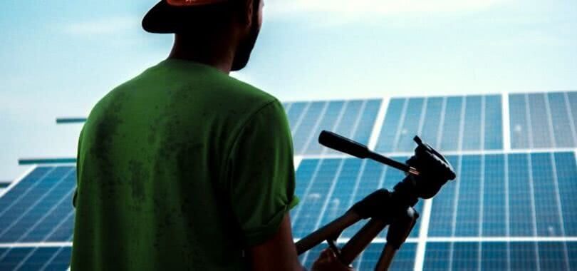 A solar photovoltaic installer holding a tool and looking out over solar panels.