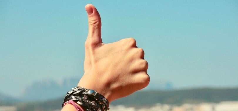 A student's hand with leather bracelets giving a thumbs up in the sky.
