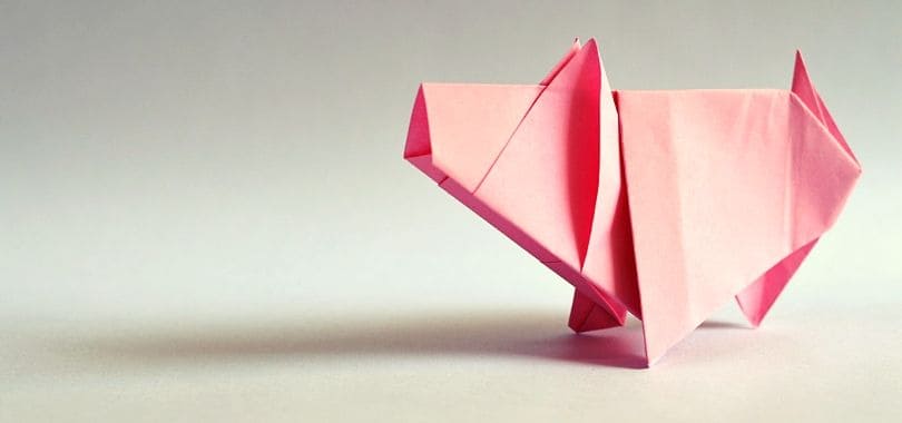 A pink origami pig standing on a gray surface.