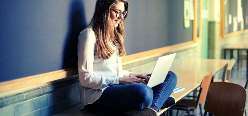 A college student sits on a desk, researching tuition insurance on her laptop.